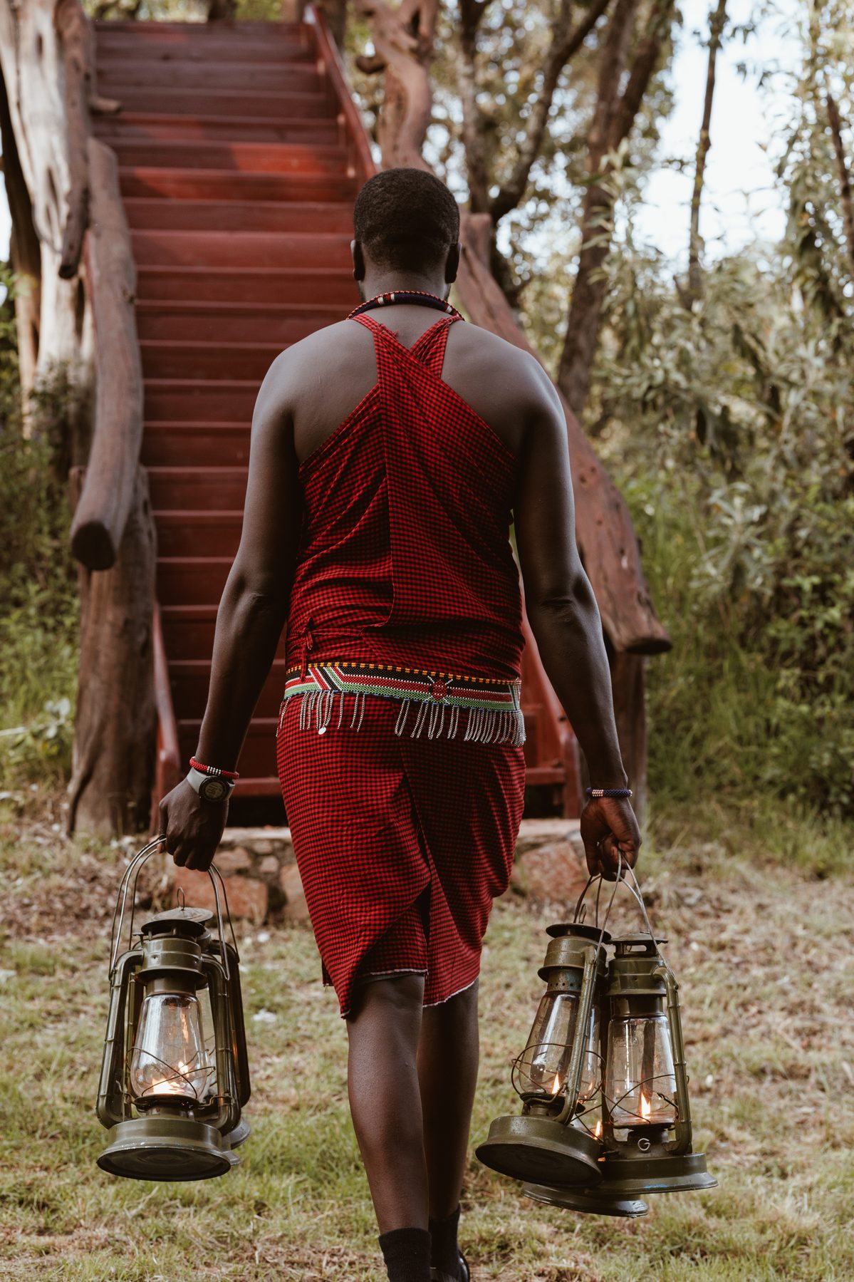 Maasai staff member carrying lanterns to a treehouse suite at dusk